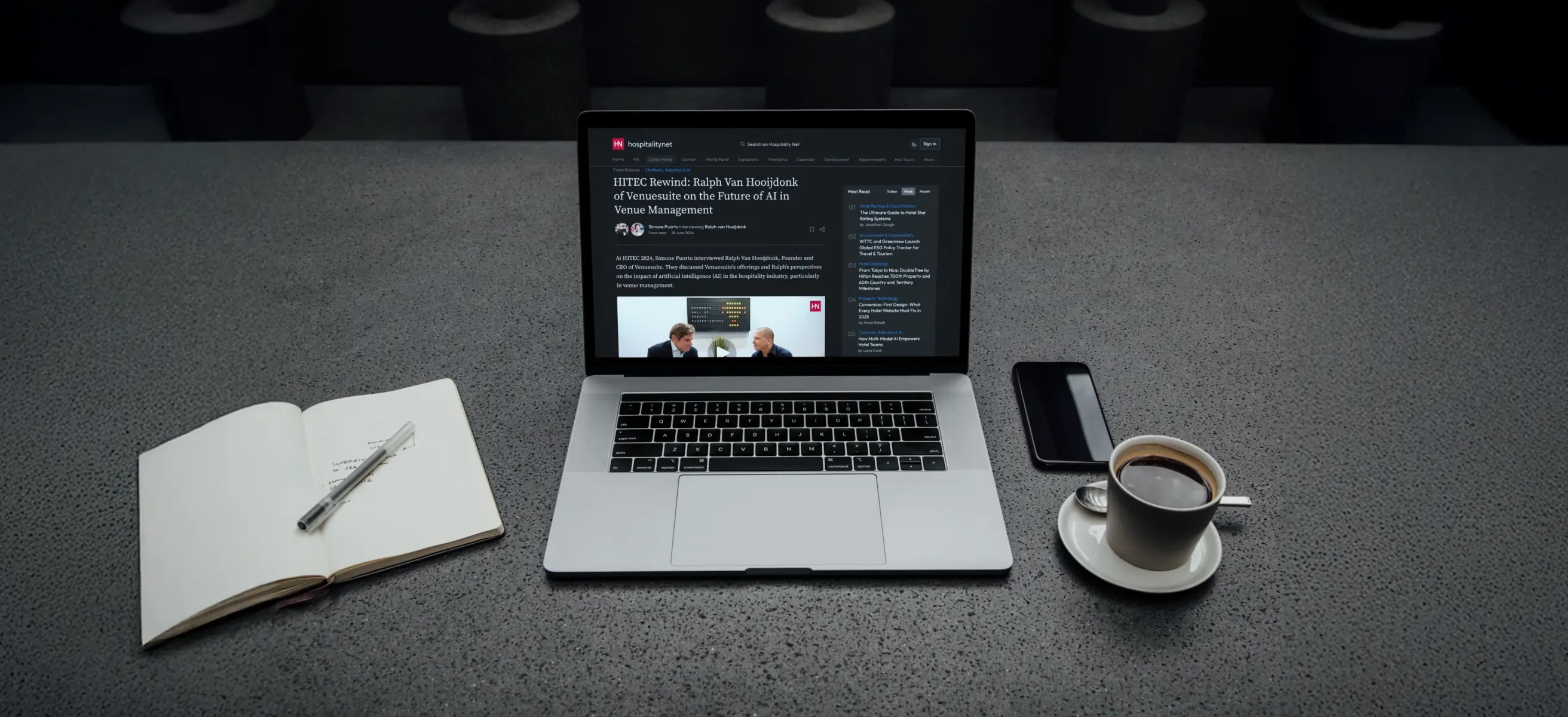 Afbeelding van een tafel met een laptop waar de webpagina van de Hospitality.net blog over AI in hospitality op staat weergegeven, kop koffie en open notitieboek.
